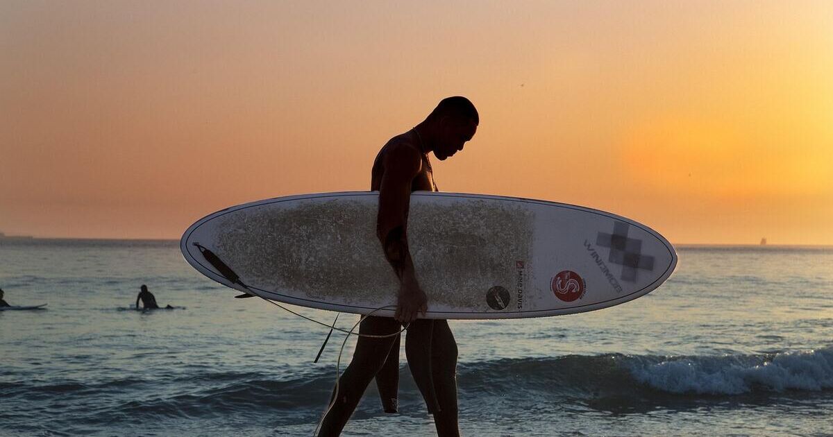 Un surfeur marche sur la plage avec sa planche au coucher du soleil