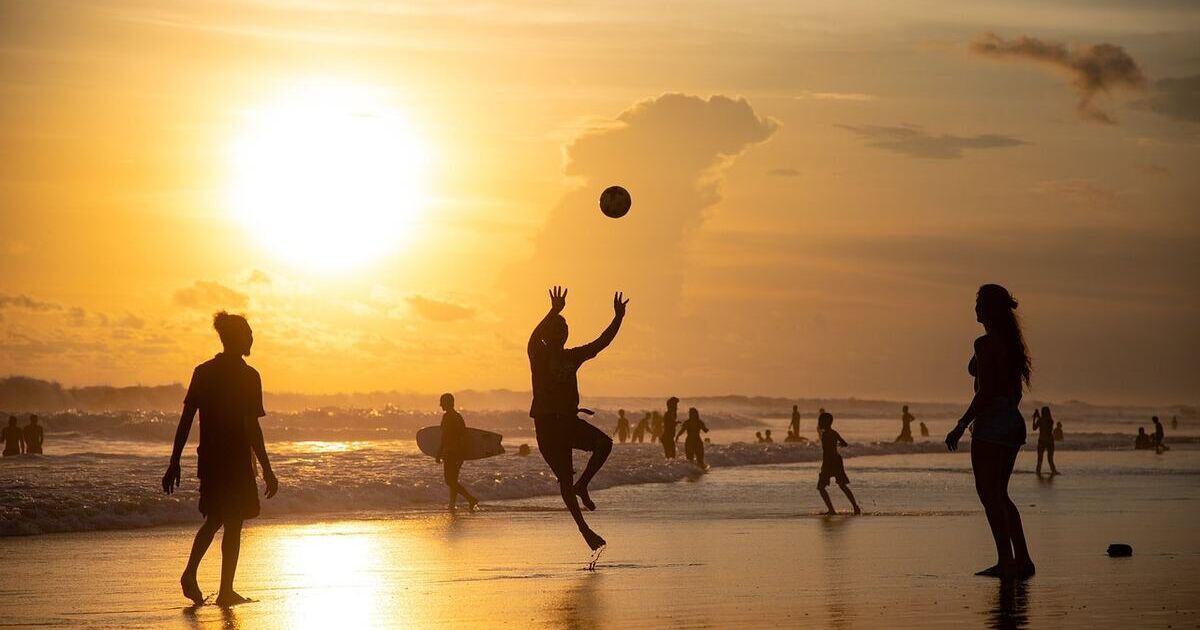 Un groupe joue au beach-volley au coucher du soleil